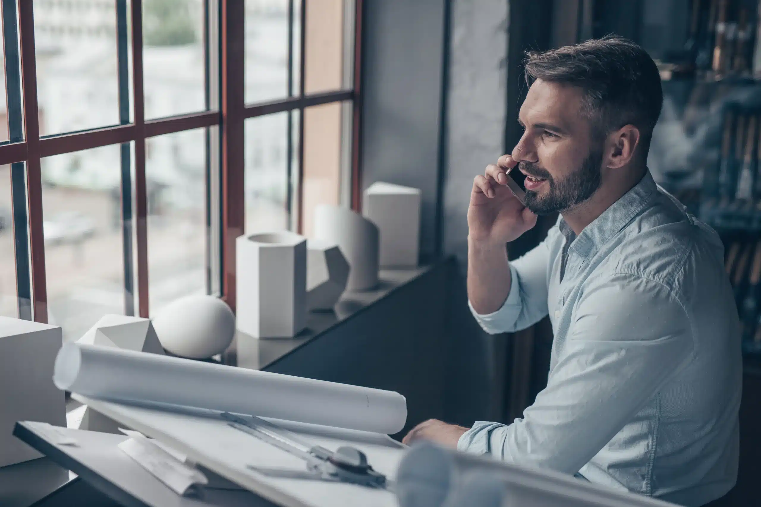6 pasos inteligentes para verificar la licencia de un Contratista en Miami-Dade 2 Profesional revisando planos y hablando por teléfono mientras coordina un proyecto de construcción o remodelación. La imagen representa la planificación, supervisión y comunicación necesarias para gestionar correctamente una obra residencial.