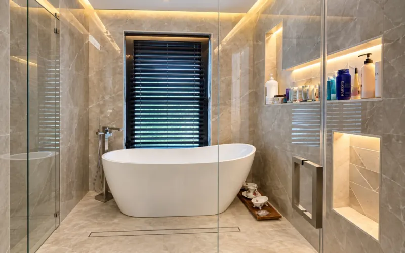 Freestanding tub next to lit niches in a stone-look surface
