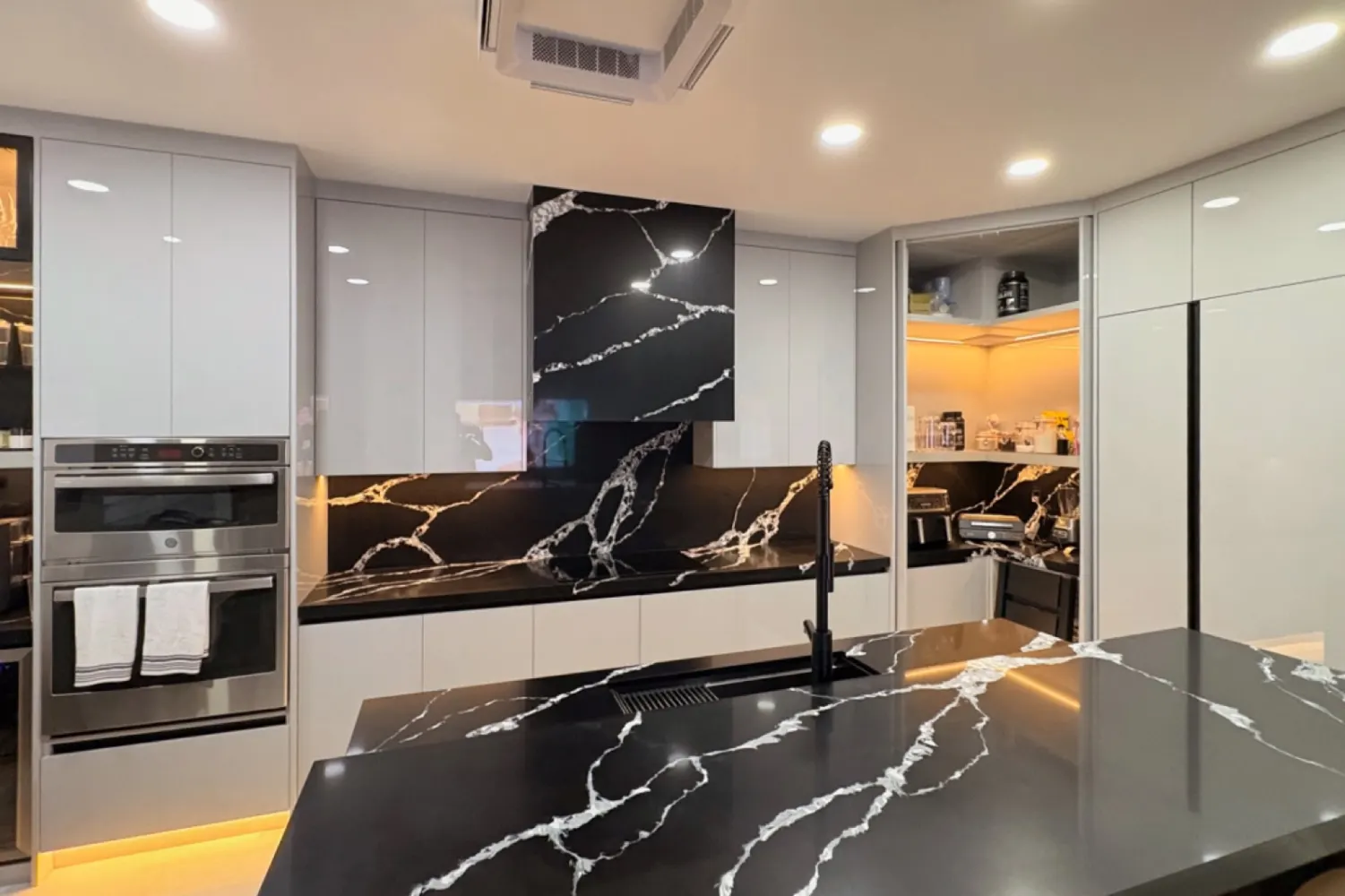 Después: gabinetes de alto brillo con countertop, backsplash y campana en piedra negra veteada