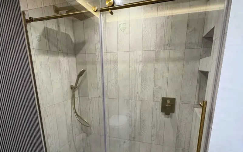 After: walk-in shower with a sliding glass door and brushed gold hardware