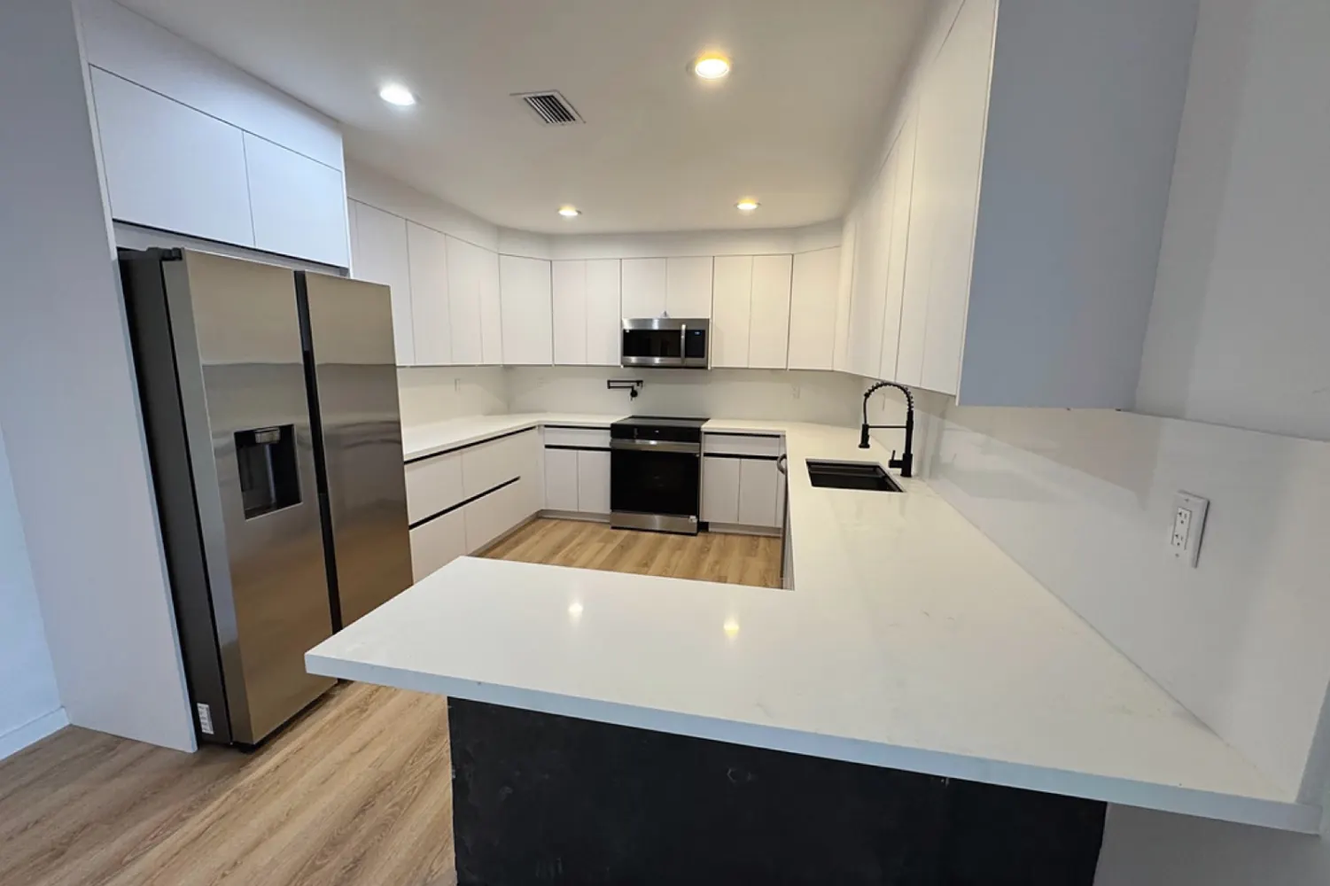 After: U-shaped kitchen with flat white cabinets, white countertop, black faucets and a wood-tone floor